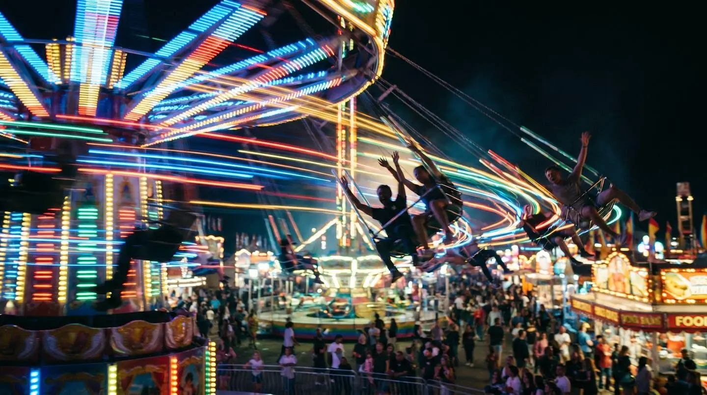 Chaises volantes en pleine rotation la nuit lors d'une fête foraine, lumières colorées et silhouettes de passagers souriants en mouvement
